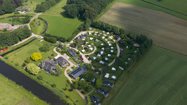 Aerial view of the Berkel river flowing through a green campsite with caravans, modern buildings, and surrounding agricultural fields in Almen, Gelderland, Netherlands.