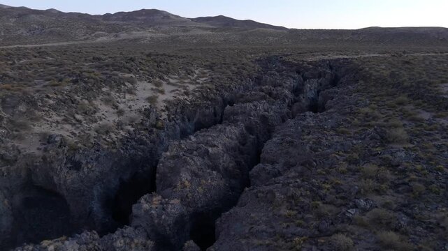 Breathtaking aerial footage of a deep volcanic rock fissure cutting through the arid landscape of La Payunia Reserve in Mendoza, Argentina.