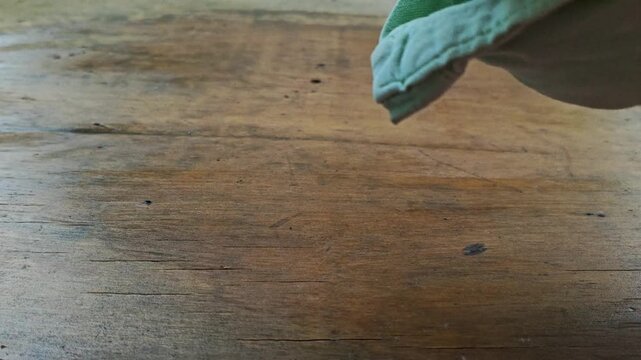 Close up of hand using cotton cloth to apply protective oil on a wood surface