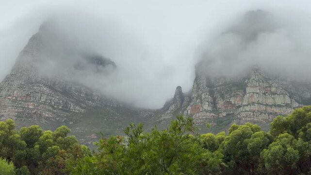 Dramatic wide shot of Table Mountain and the Twelve Apostles mountain range enveloped in thick rolling cloud and mist, Cape Town, South Africa. The iconic sandstone cliff faces and rocky outcrops.