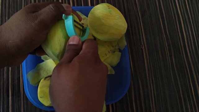 Hands peeling ripe yellow mangoes using a rustic kitchen knife