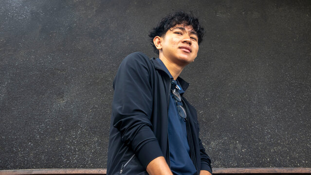 young man wearing black jacket sitting against black wall