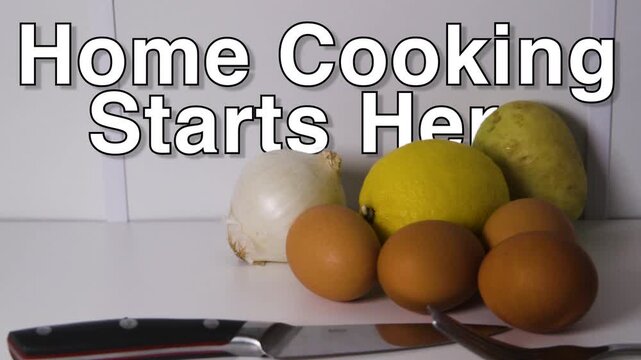 Home Cooking Starts Here text sits over raw staples including eggs, lemon, potato, onion, fork and chef knife on a plain surface.