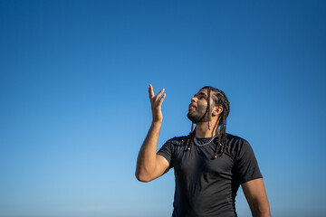 Fototapeta premium Young man looking up with hand raised feeling freedom