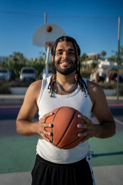 Confident young man with braids holding basketball on outdoor court