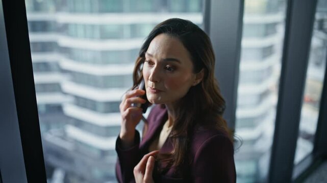 Wealthy business lady calling mobile phone standing at office window closeup