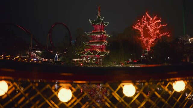 Asian pagoda with christmas lights at night in amusement park reflecting on water surface slow pan.