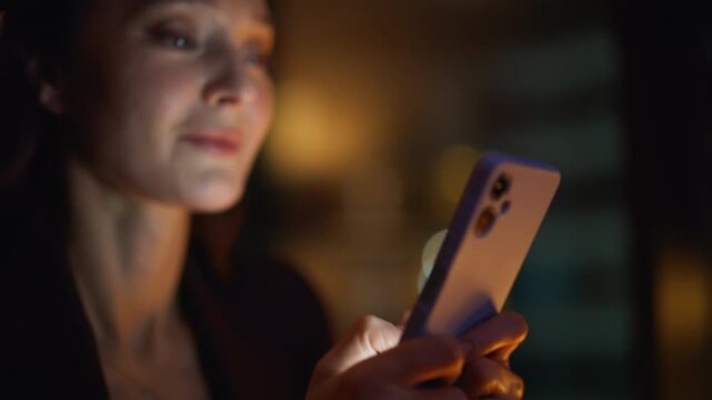 Night manager messaging cellphone with lamp light closeup. Woman hands texting