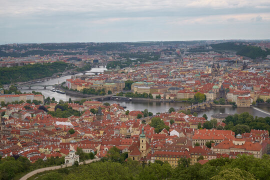 High-angle panoramic view of Prague, featuring the Vltava River bending through the historic city with its characteristic red rooftop architecture.