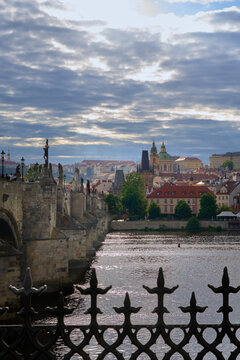 View of the historic Charles Bridge in Prague, shot through an ornate iron fence with Prague Castle in the background.