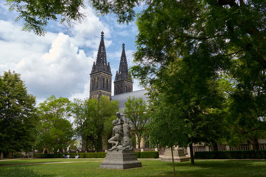The twin spires of the Basilica of St. Peter and St. Paul rising above a lush green park in the historic Vysehrad fortress, Prague.