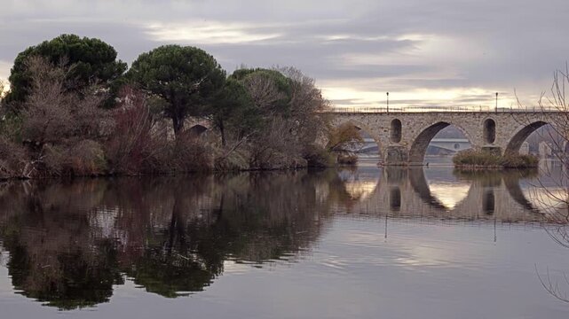 Masonry Pointed arch Stone bridge (Puente de Piedra) across the river Duero in Zamora, Castile-Leon, Spain. Reflection in the water. Autumn nature. Pedestrians walking on the bridge. Overcast.