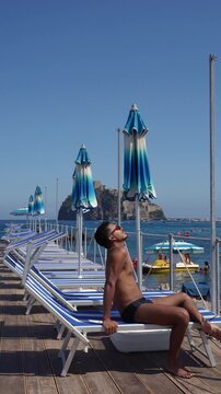 Young man relaxing at an Italian beach club overlooking Castello Aragonese in Ischia