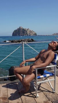 Young man relaxing by the Mediterranean Sea with Aragonese Castle in Ischia