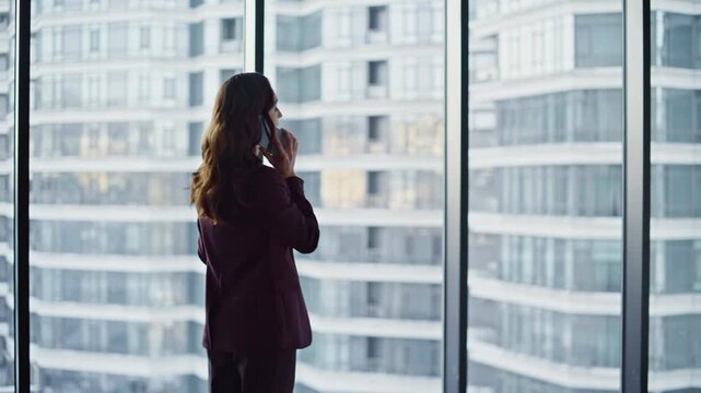 Business manager speaking cellphone standing at panoramic window luxury office