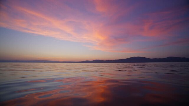 Peaceful sunset view from a boat on Lake Geneva, Switzerland. Pink clouds stretch across the sky above calm water and distant mountain silhouettes near the Jura.