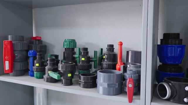 Static medium shot of a warehouse shelving unit displaying a variety of industrial plumbing components, PVC pipe fittings, and manual ball valves for water irrigation and supply systems