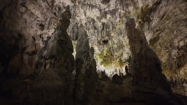 Huge cavern with illuminated ancient stalactites hanging from the ceiling and large stalagmites rising from the floor in a dark cave