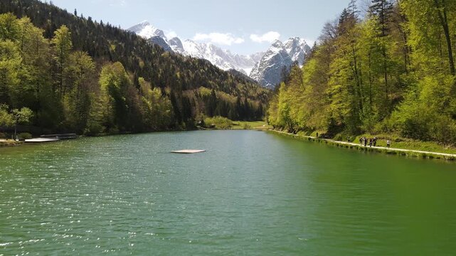 Hintersee lake in Ramsau, Bavarian Alps. Runners on the lakeshore trail with Reiter Alm mountains in background. Scenic alpine nature footage, outdoor sports activity in Germany.