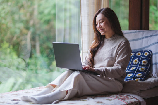 Portrait of a woman using and working on laptop computer while sitting on bed at home