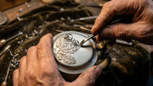Macro view of German beer stein engraver hand carving pewter metal lid relief pattern steel graver