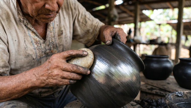 Mexican black pottery master burnishing wet clay pot smooth quartz river stone Oaxaca photo