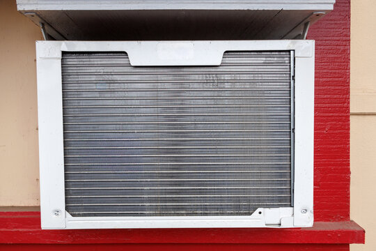 Close up shot of a window air conditioning unit showing its metallic cooling fins and outer frame installed on a building wall