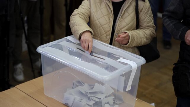 Voters cast their votes at a voting station. Transperant plastic ballot box.