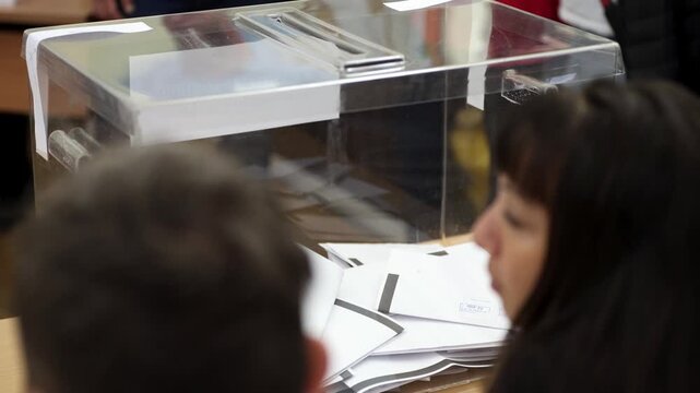 Voters cast their votes at a voting station. Transperant plastic ballot box.
