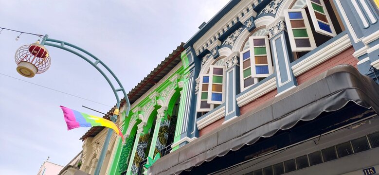 Low angle view of colorful Sino-Portuguese building decorated with rainbow pride flag and traditional lantern in Phuket Old Town.