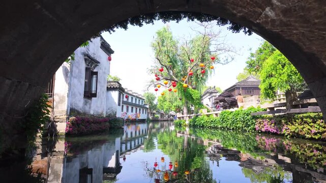 A view from beneath a stone bridge in Zhouzhuang reveals colorful lanterns and reflections on the canal. Ideal for cultural documentaries or travel features.
