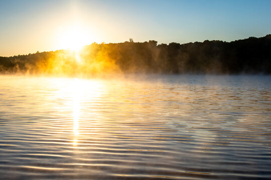 Blazing dawn slips above the ridge and gilds the mist that hovers over a glassy river while delicate waves spread outward and the softened forest rests in silence awaiting gentle movement of day