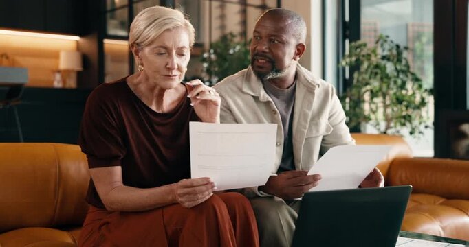 Documents, laptop and stress with interracial couple on sofa in home living room for debt or tax. Anxiety, computer and paperwork with mature people in apartment for financial argument or conflict