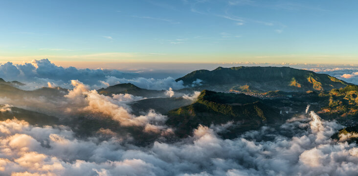 Aerial view of the mountainous landscape near Basecamp Gunung Bismo via Sikunang, featuring lush green slopes, rolling hills, and a sea of clouds in Kecamatan Kejajar, Jawa Tengah, Indonesia.