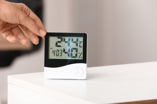 Hand adjusting digital thermometer and hygrometer on table