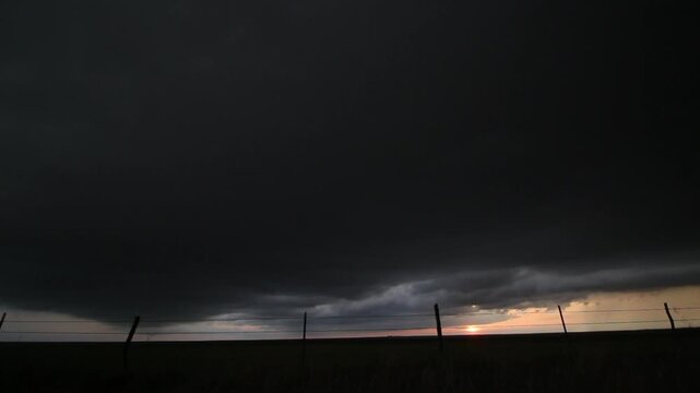 A large, dark shelf cloud moves overhead as the sun sets on the prairie. Time lapse footage.