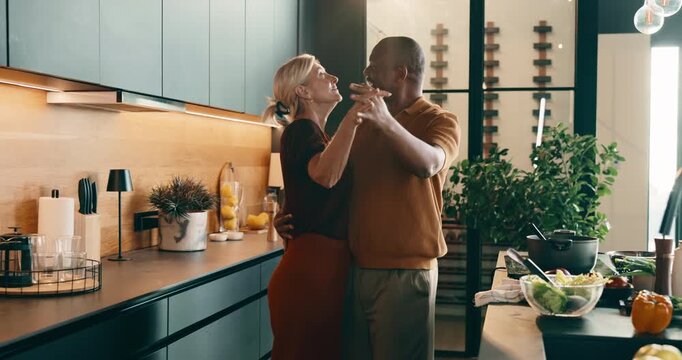 Happy, dancing and holding hands with food in kitchen for meal prep, fun cooking or vibe together. Interracial couple, love or smile with mature people for weekend, dinner or bonding in house