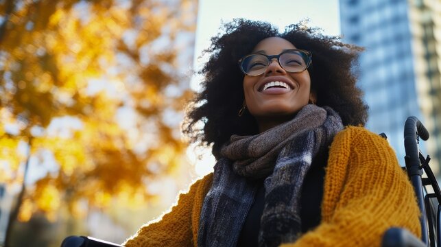 Joyful Autumn Ride: A woman in a wheelchair smiles joyfully amidst the warm hues of autumn, with golden leaves and urban buildings forming a vibrant backdrop.