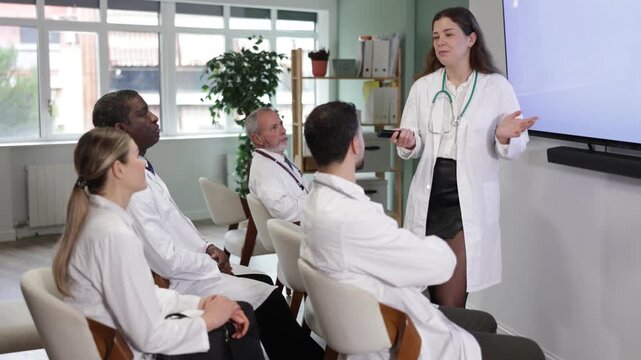 Young female doctor holds a remote control rod in her hands and gives a lecture in front of other doctors in the audience. . High quality 4k footage