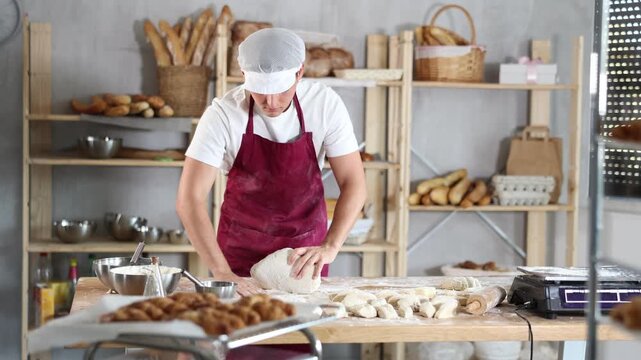  Working in a bakery - guy kneads raw dough to make baguettes or croissants