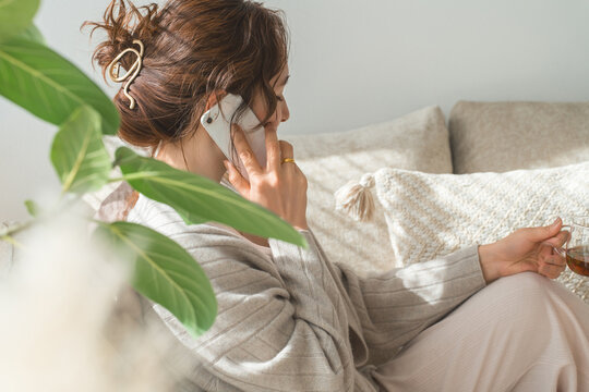 A stylish woman sitting on a sofa and talking on her smartphone.