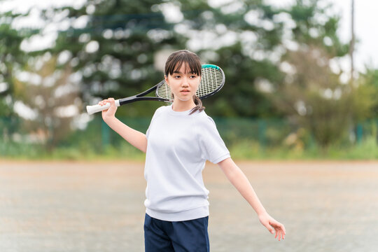 Elementary, middle, and high school girls in gym clothes playing tennis on the school grounds.
