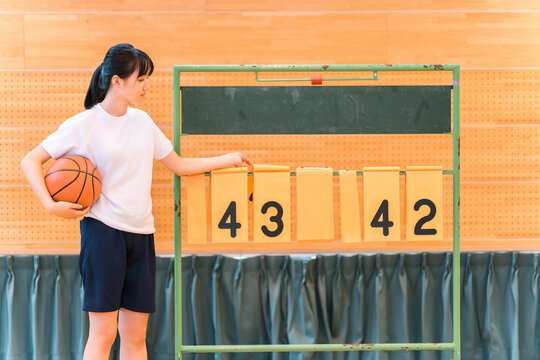 A female student in gym clothes flips over the scoreboard in the gymnasium.