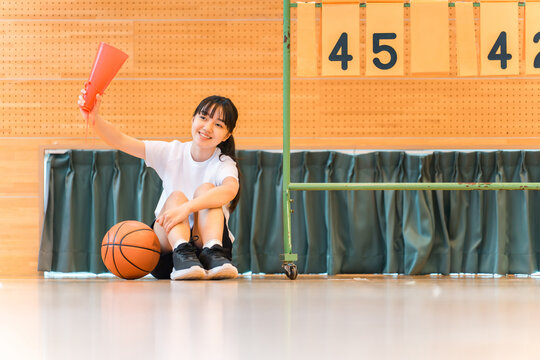 A female student cheering on her school club, the basketball team, at a sports festival, class match, tournament, or game.