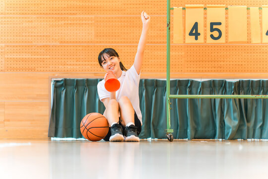 A female student cheering on her school club, the basketball team, at a sports festival, class match, tournament, or game.