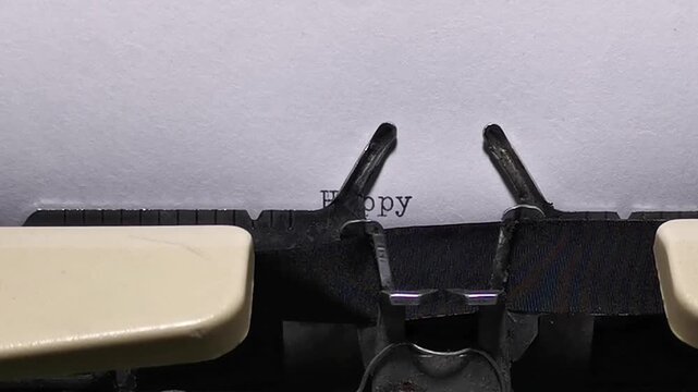 Close-up shot of an old mechanical typewriter in action, typing a Happy Anniversary message letter by letter. The typebars strike the black ink ribbon to print on a blank sheet of paper, creating a no