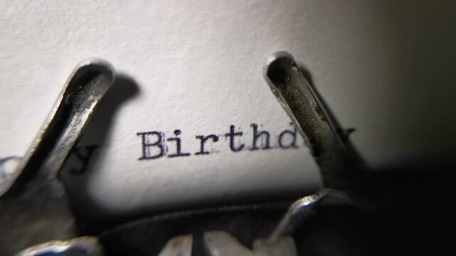 Close up macro shot of an antique typewriter typing the words Happy Birthday on white paper.