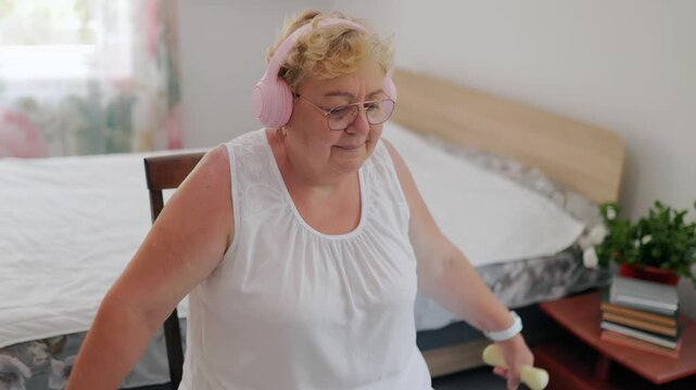 Mature overweight female doing fitness, straining while doing lateral dumbbell raises indoors