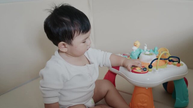 Cute little baby boy sitting on a play mat, touching and exploring colorful learning toys.