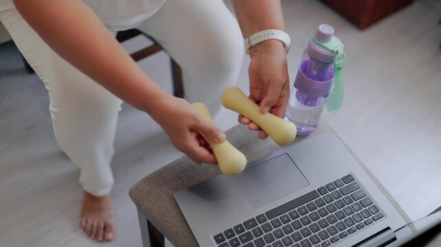 Top view of mature woman hands picking up yellow weights at home desk fitness at home